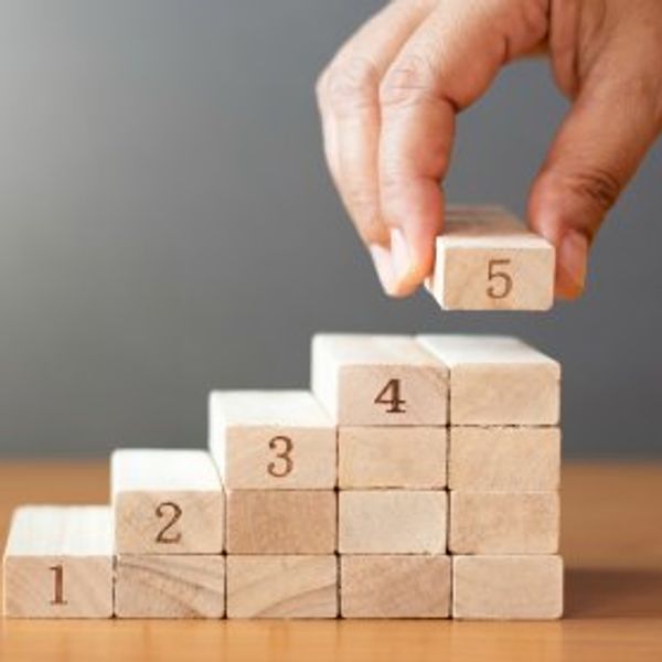 Hand stacking wooden blocks numbered 1 to 5 in staircase form.
