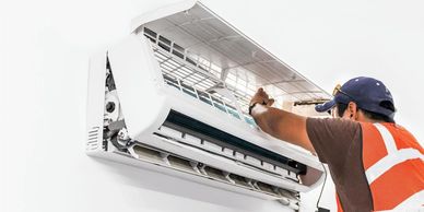 Technician repairing a wall-mounted air conditioner indoors.