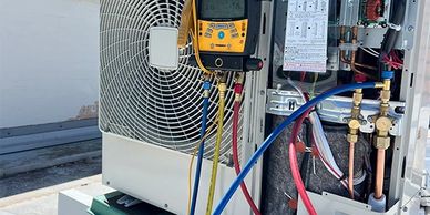 Technician testing an air conditioning unit with diagnostic tools on a rooftop.