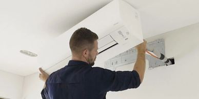 Technician installing a wall-mounted air conditioner indoors.