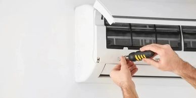 A person repairing an air conditioner with a screwdriver.