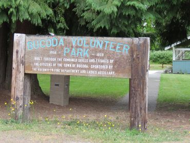 Wooden sign for Bucoda Volunteer Park in a green park setting.