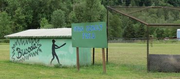 Small baseball field with a green wall and a sign reading 'Tom Ozbolt Field'.