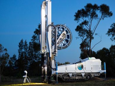 A tall, white drilling machine with a circular component on a tracked base outdoors.