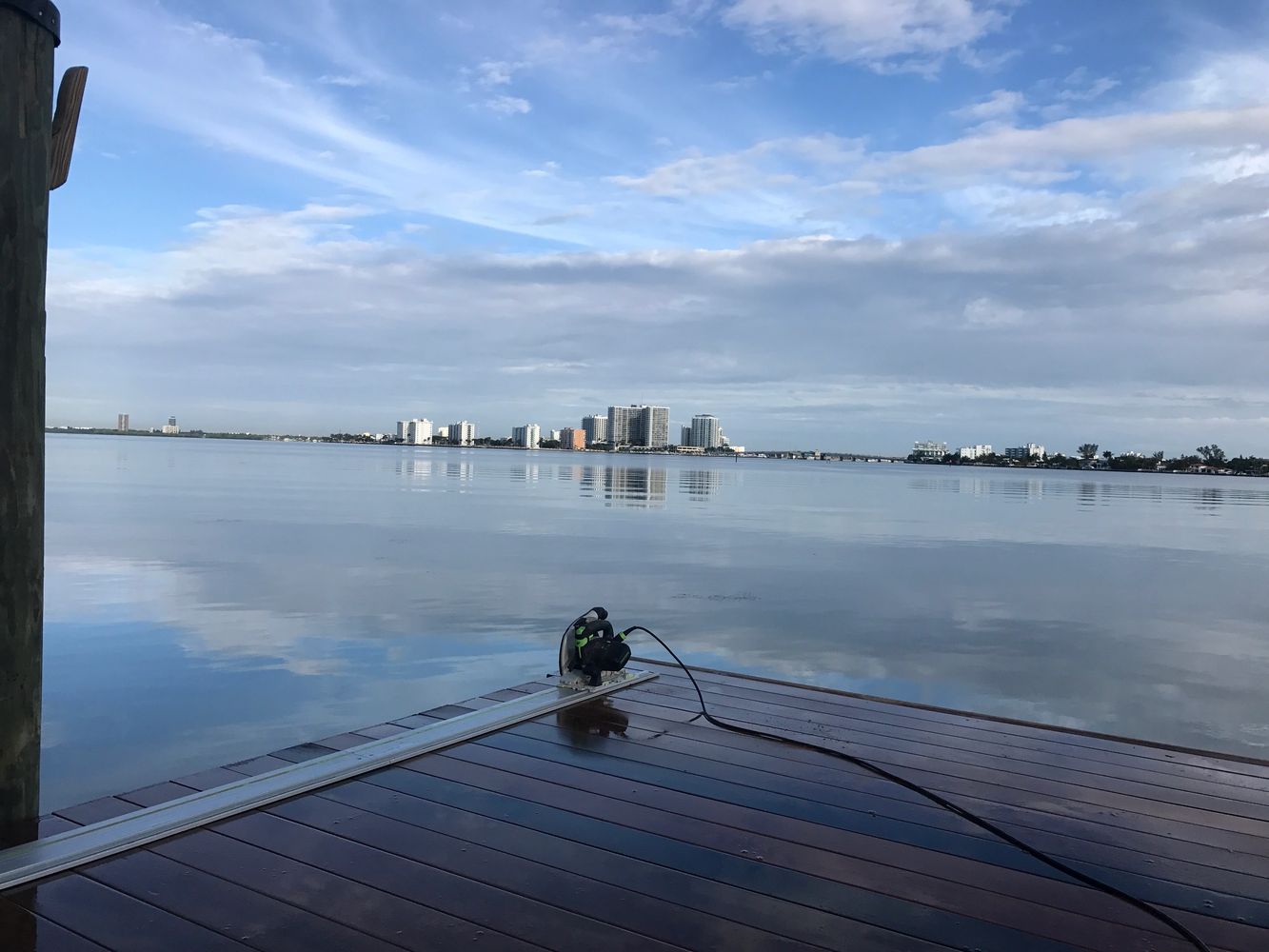 Hardwood waterfront deck in Miami with a floor polisher on the boards and metal edge trim, looking out over Biscayne Bay. Shows coastal-grade deck installation and maintenance.