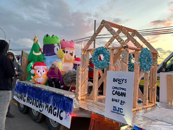 Holiday float featuring a Christmas cabin and inflatable characters.