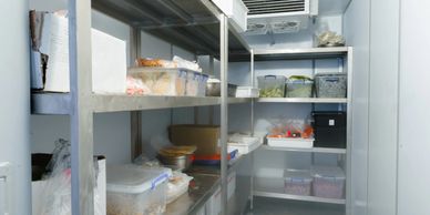 A clean, organized walk-in refrigerator with shelves storing various food containers.