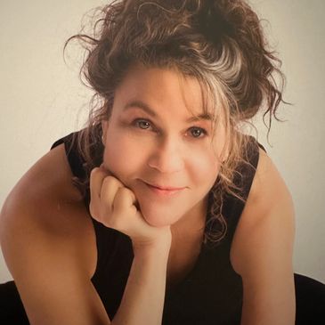 Smiling woman with curly hair resting her chin on her hand.