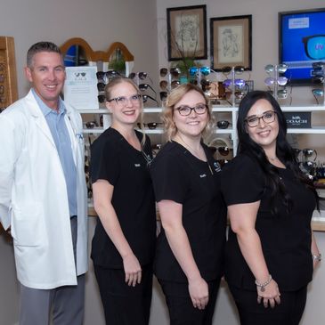 Four optometry professionals smiling in an eyewear store.