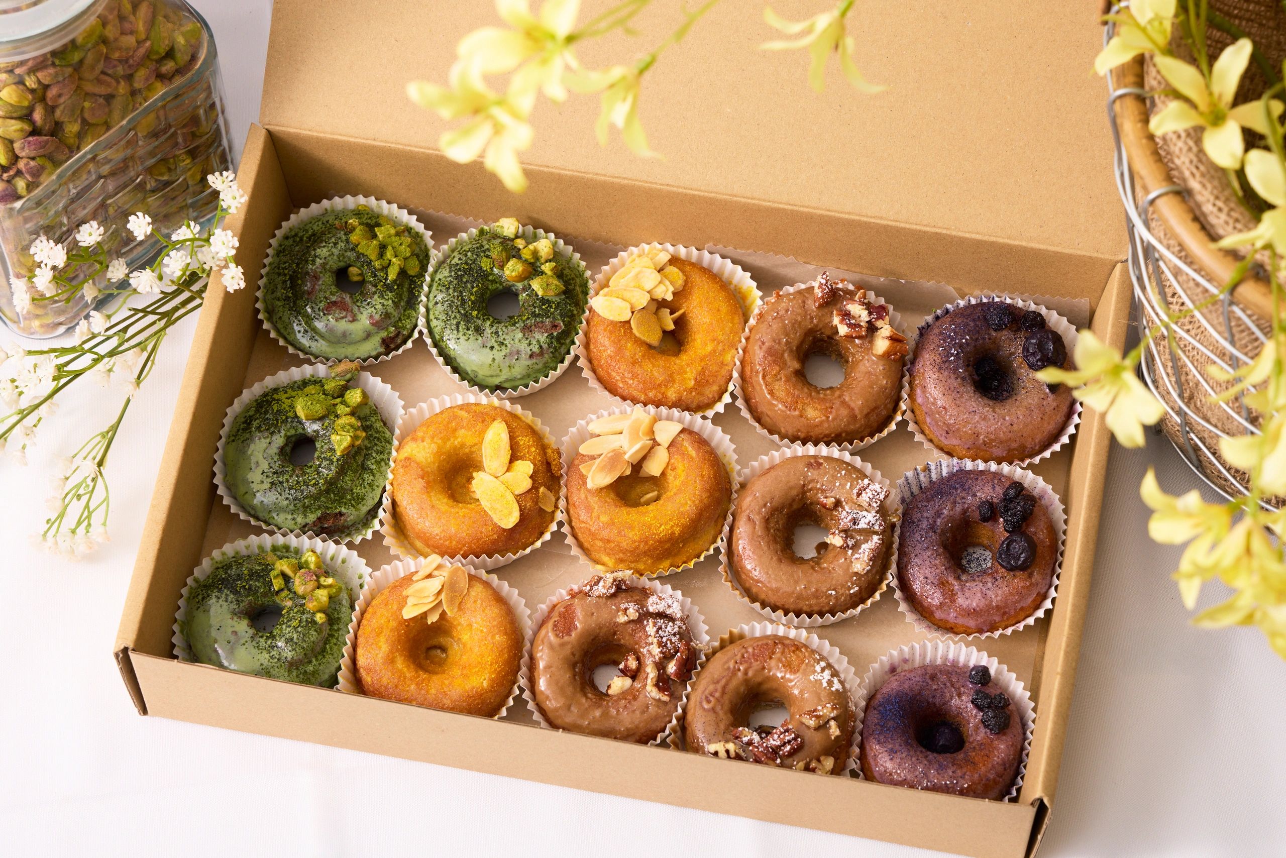 Assorted gourmet donuts in a box, decorated with nuts and berries.