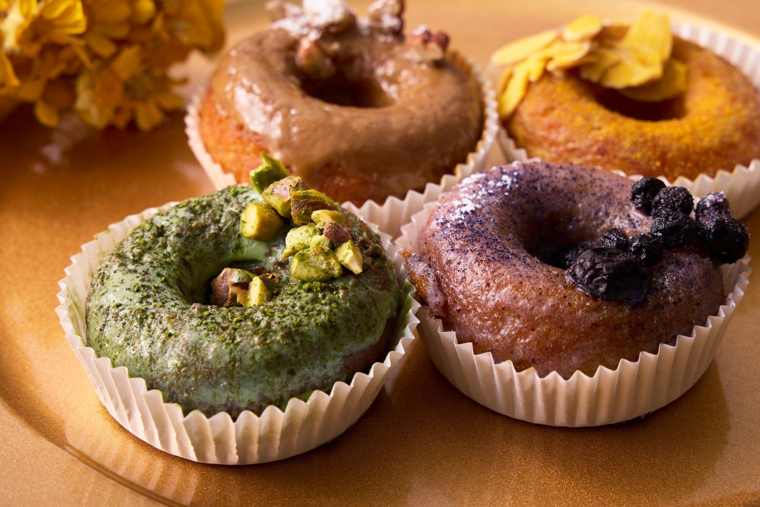 Four gourmet donuts with unique toppings displayed on a golden plate.