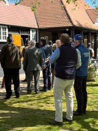 People gathered outdoors near a wooden building on a sunny day.