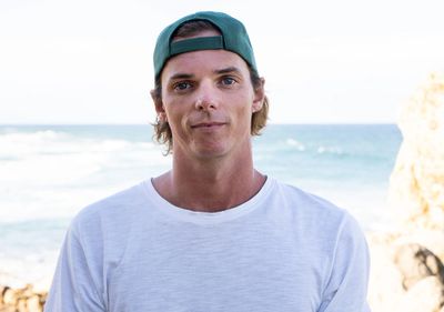Young man wearing a backward green cap and white shirt by the beach.