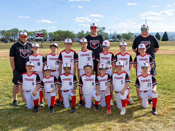 Youth baseball team Tribe posing with coaches outdoors on a sunny day.