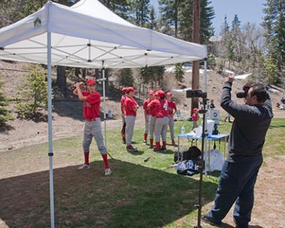 Young baseball players practicing batting under a tent in a park.