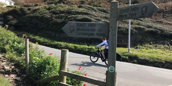 Cyclist riding near coast path signs on a sunny day.
