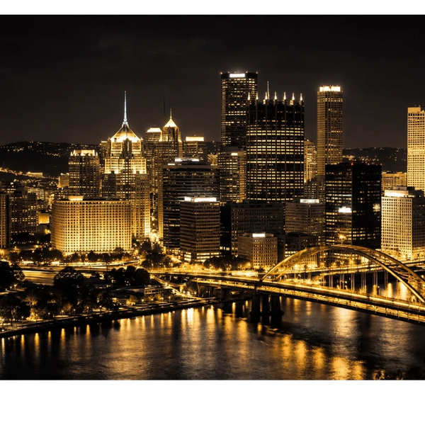 Night skyline of a city with illuminated buildings and a glowing bridge over water.