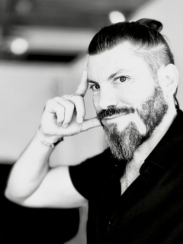 Black and white portrait of a man with a beard and tied hair.