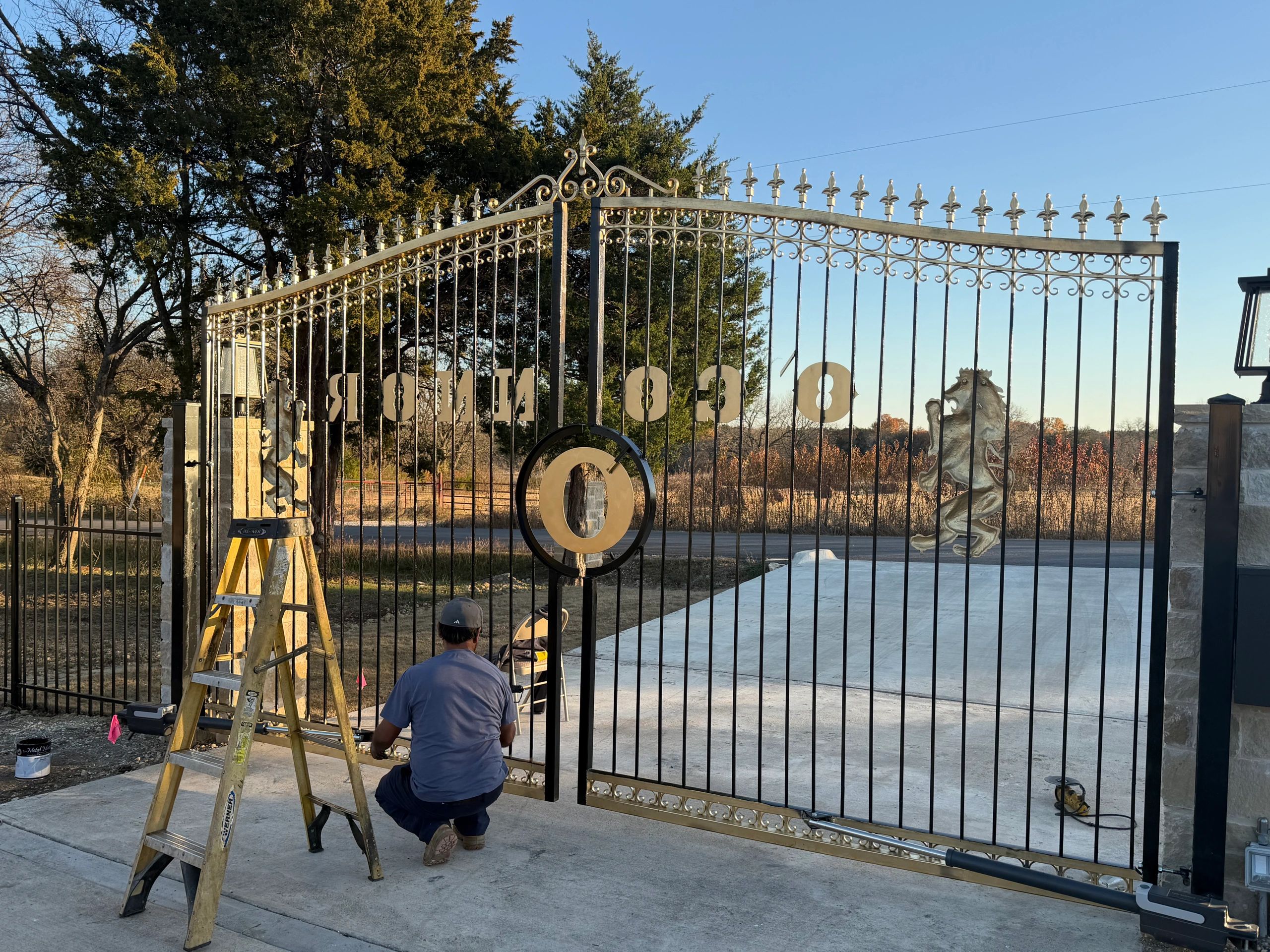 Person working on a large ornate metal gate at sunset.
