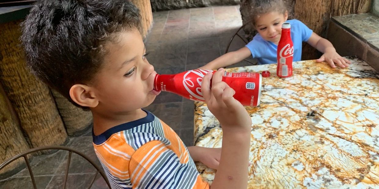 Two children drinking Coca-Cola at a marble table.