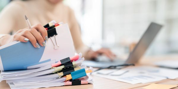 Person organizing thick paperwork with binder clips while using a laptop.