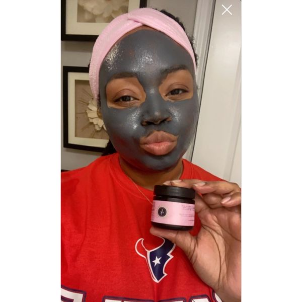 Woman with a charcoal face mask holding a skincare product jar.