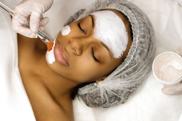 A woman receives a facial mask treatment at a spa, eyes closed and relaxed.