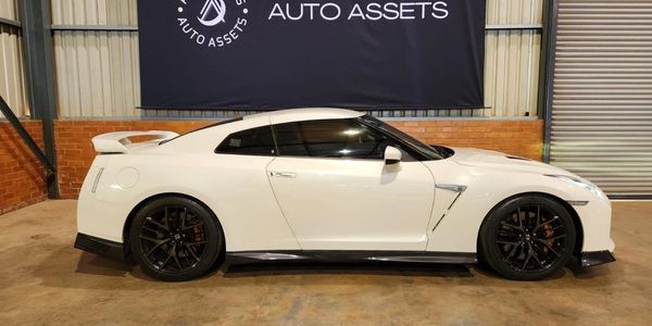 White sports car parked indoors with black rims and spoiler.