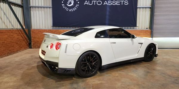 White Nissan GT-R sports car parked indoors with black wheels and tinted windows.