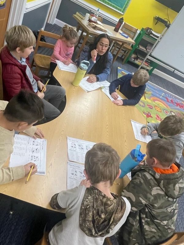 Teacher helping kids with schoolwork around a table.