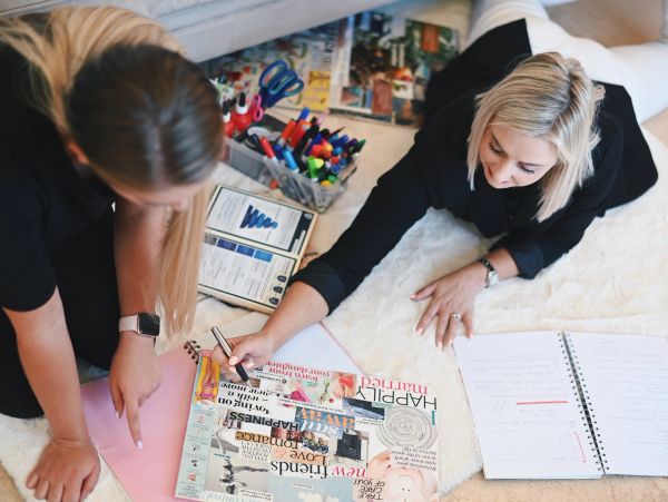 Two women working on a collage and notes on the floor.