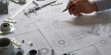 Engineer reviewing technical mechanical drawings with tools and parts.