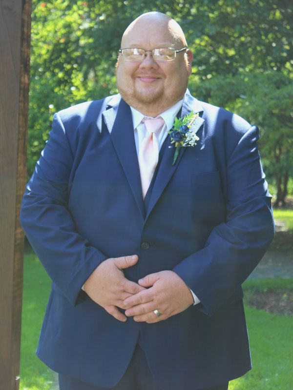Smiling man in suit with boutonniere outdoors.