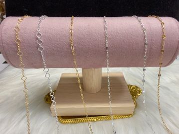 Elegant gold and silver chain necklaces displayed on a pink stand.