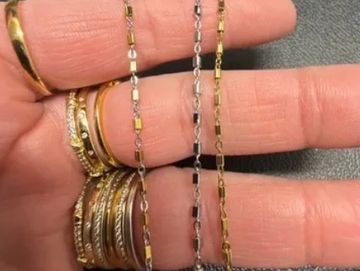 Hand displaying gold rings and delicate gold and silver chains.