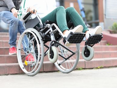 A person in a wheelchair being pulled backwards up a flight of stairs by another person