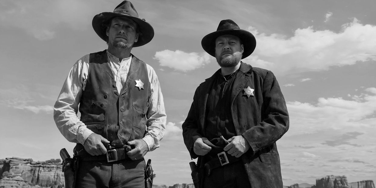 Two sheriffs in cowboy hats stand ready in a desert landscape.