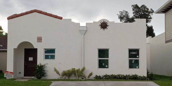 Small white house with a dark door and three windows.