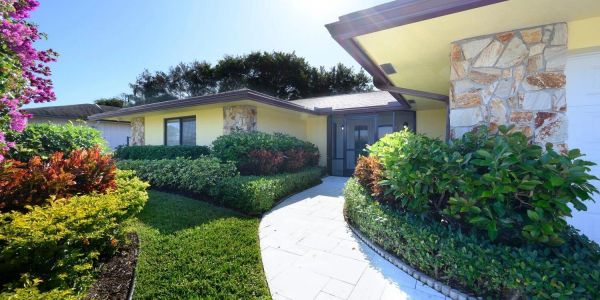 Sunny entrance to a yellow house with lush greenery.