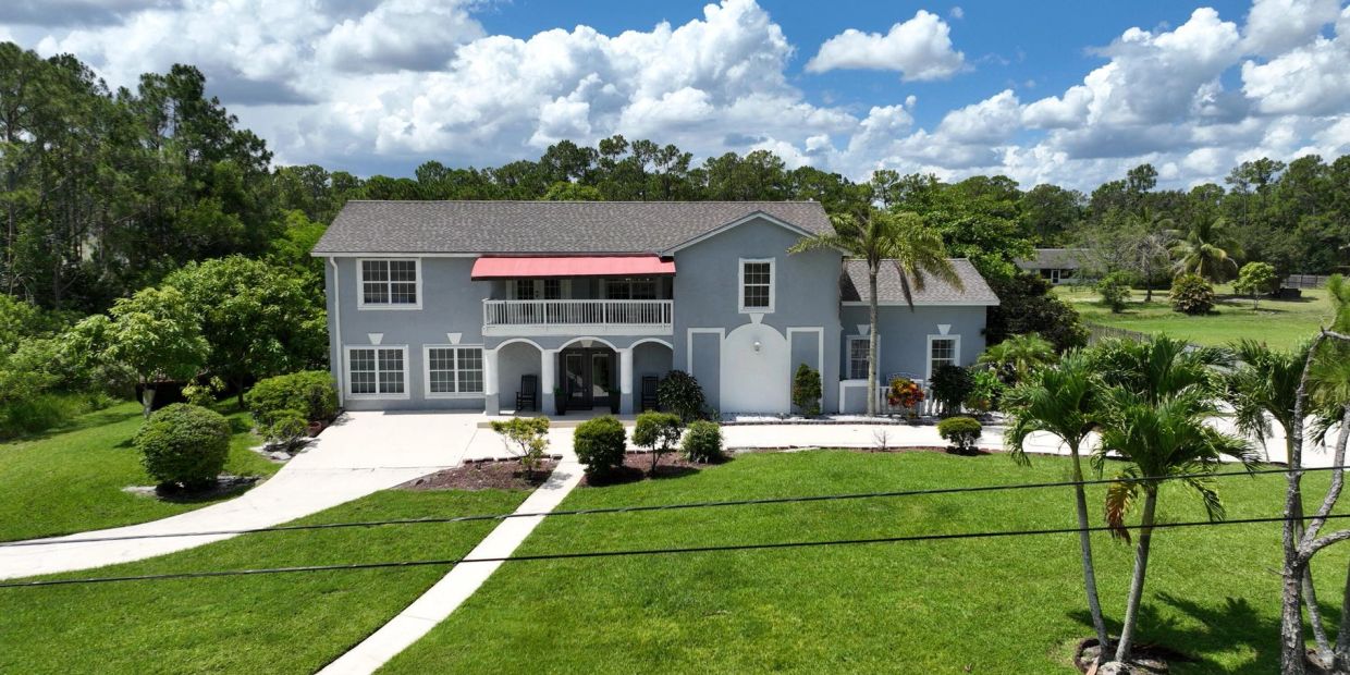 Large two-story house with a bright red awning and lush green lawn.