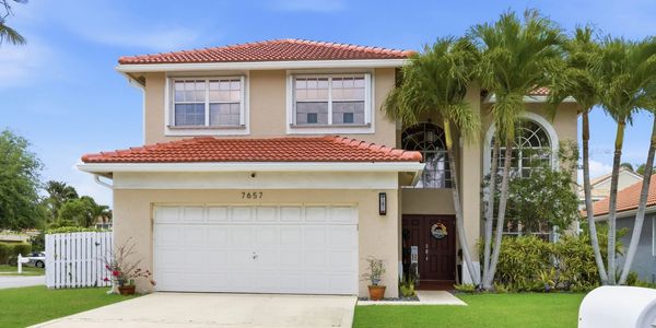 Two-story beige house with a red tile roof and palm trees.
