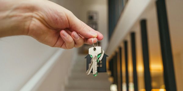Hand holding house keys inside a modern home with staircase.