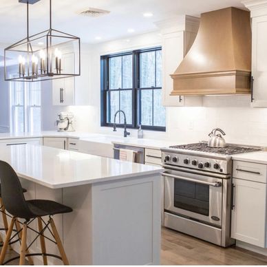 Modern white kitchen with island, black chairs, and stainless steel appliances.