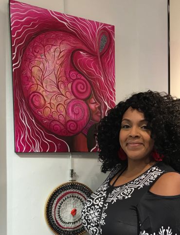 Woman posing beside vibrant pink afro-themed artwork and a circular woven decoration.