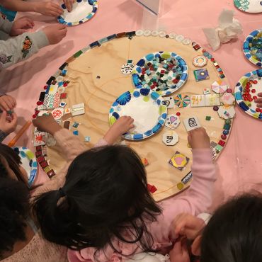 Children decorating a circular board with colorful tiles and beads.