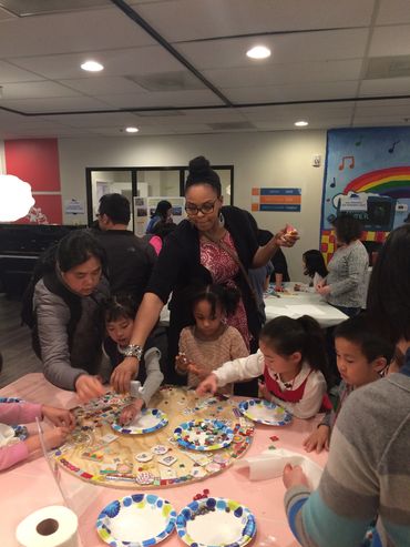 Adults and children engaged in a group craft activity around a table.