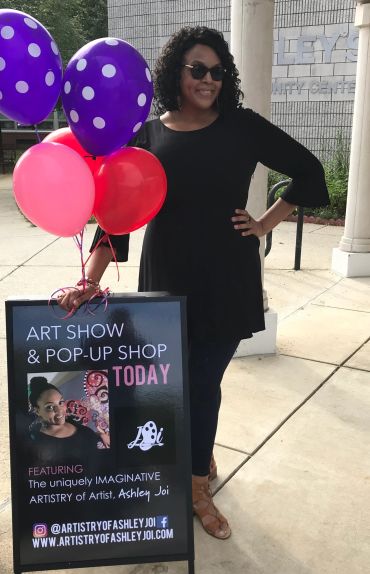 Woman posing next to an art show sign with colorful balloons.