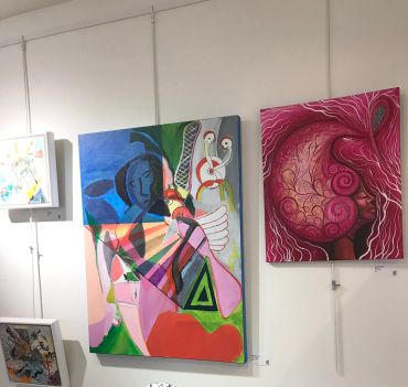 A gallery wall with colorful abstract and surreal paintings on display.