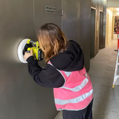 Person polishing a metallic wall with a power buffer.