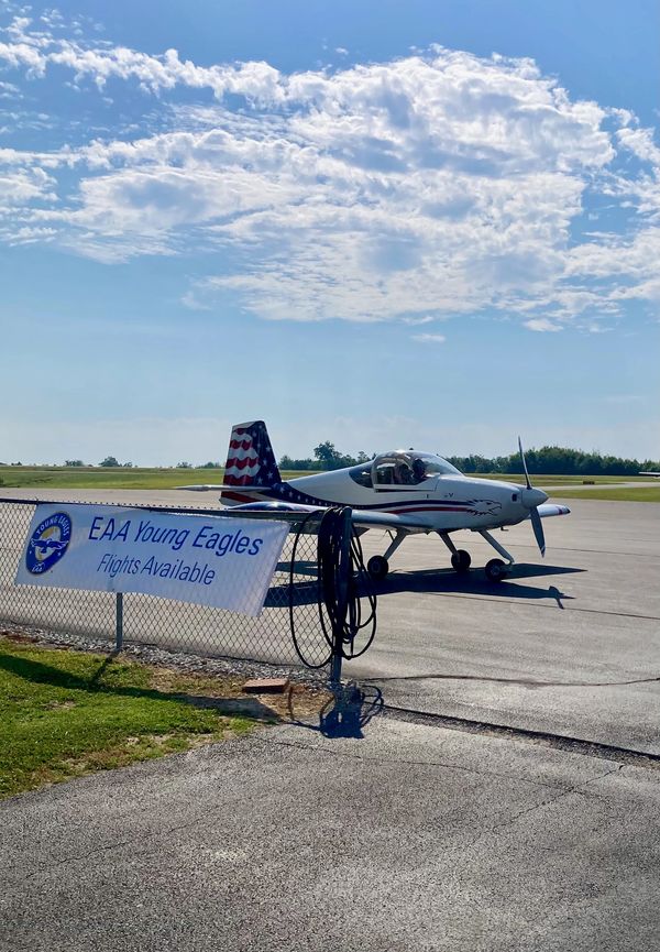 Small airplane parked near a sign for EAA Young Eagles flights on a sunny day.
